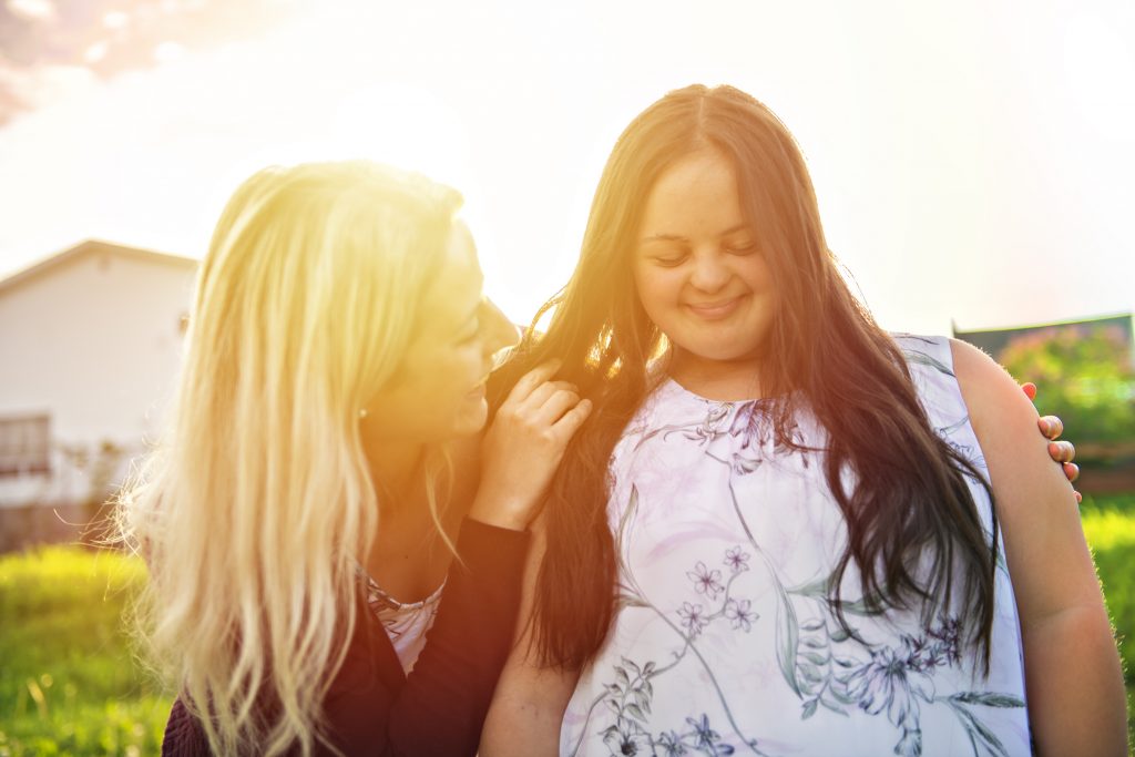 A Portrait of trisomie 21 adult girl smilin outside at sunset with family friend