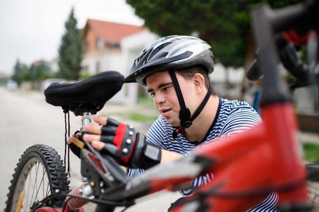 Portrait of down syndrome adult man with bicycle standing outdoors on street, repairing.